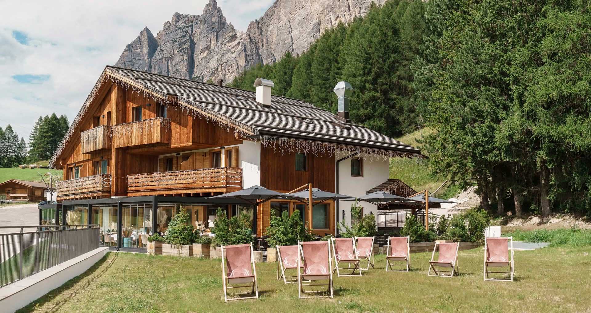 Facciata esterna Casa Guargnè Cortina d’Ampezzo durante l'estate con prato verde e sdraio